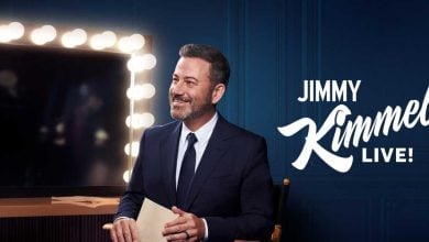 A man in a suit sits smiling with an envelope in hand, next to a lit vanity mirror. The text "JIMMY KIMMEL LIVE!" appears beside him on a dark blue background.