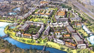 A colorful aerial illustration of a planned mixed-use community with apartment buildings, green spaces, tree-lined streets, and a river curving around the development; roads and highways are visible in the background.