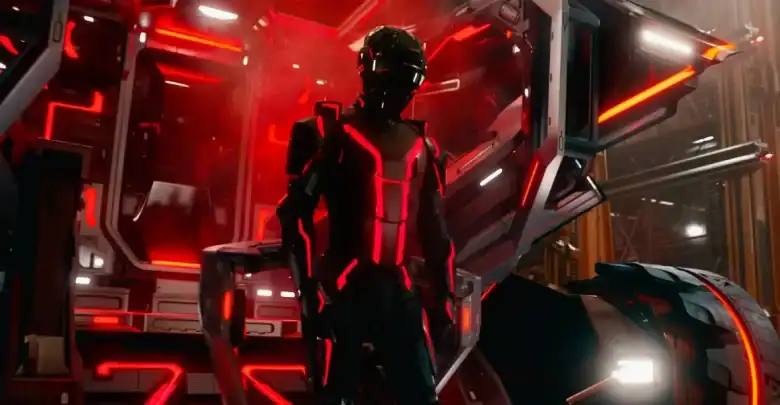 A person in a futuristic black and red illuminated suit stands before a high-tech structure with glowing red lights and angular metallic panels, evoking the iconic sci-fi atmosphere of a Disney Tron advertisement.