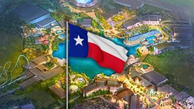 An illustrated aerial view of a theme park at night, brightly lit with various buildings and rides, with a large Texas state flag prominently displayed in the center.