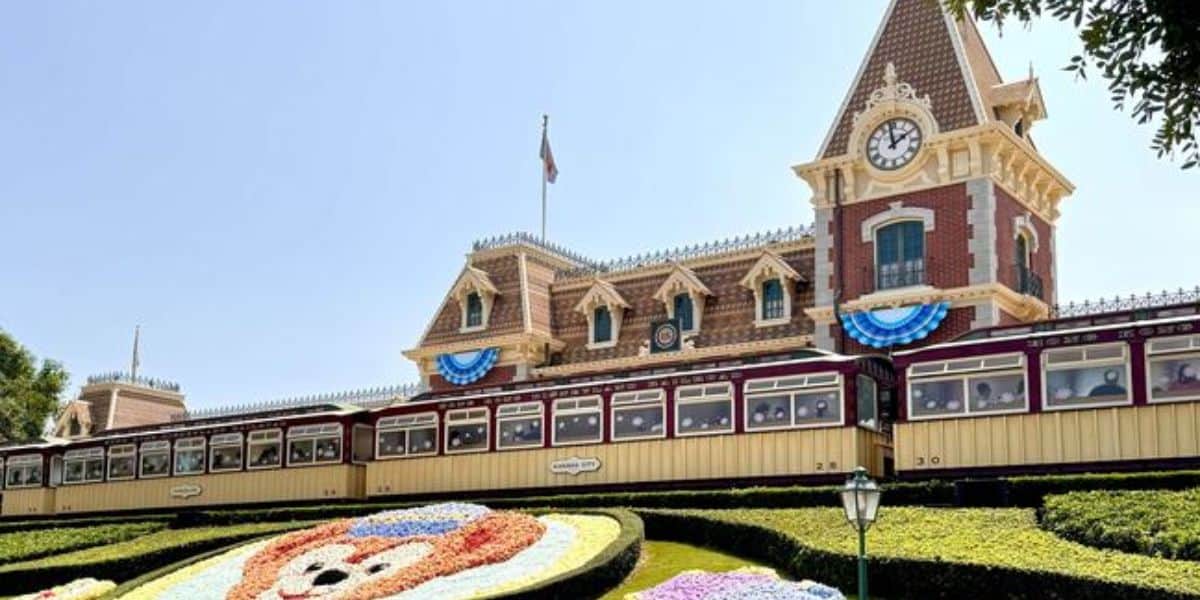 The Disneyland Train Stationās clock tower, bunting, and floral Mickey faceāan iconic welcome for Disney Annual Passholders.