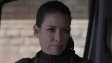 A woman with dark hair pulled back, in a dark jacket, sits in a ride vehicle, focused like an MCU actor on set.