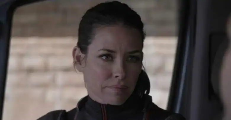 A woman with dark hair pulled back, in a dark jacket, sits in a ride vehicle, focused like an MCU actor on set.