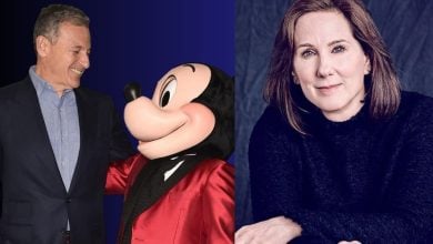 A happy guest smiles at Mickey Mouse in a dapper red tux, while a woman with light brown hair sits nearby, looking at the camera.