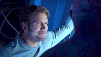 A guest in a Captain America tee grins by a blue Marvel wall, chatting about Avengers plots with another fan in dramatic lighting.