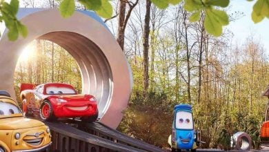 Lightning McQueen, Mater, and Cruz Ramirez race on a toy track with a giant loop, surrounded by trees and sunshine.