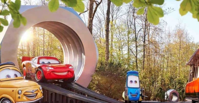 Lightning McQueen, Mater, and Cruz Ramirez race on a toy track with a giant loop, surrounded by trees and sunshine.