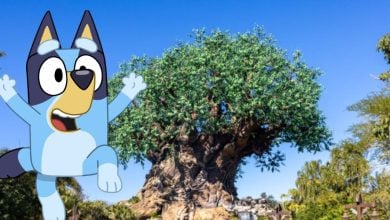 Bluey leaps playfully before a grand tree in Australia Land’s Animal Kingdom, set against blue skies and vibrant greenery.