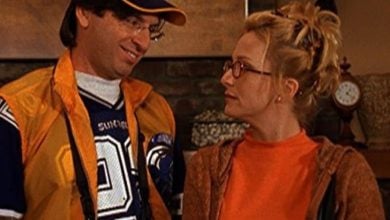 A sports-clad guest beams at a woman in glasses and an orange sweater, capturing Disney Channel nostalgia indoors.