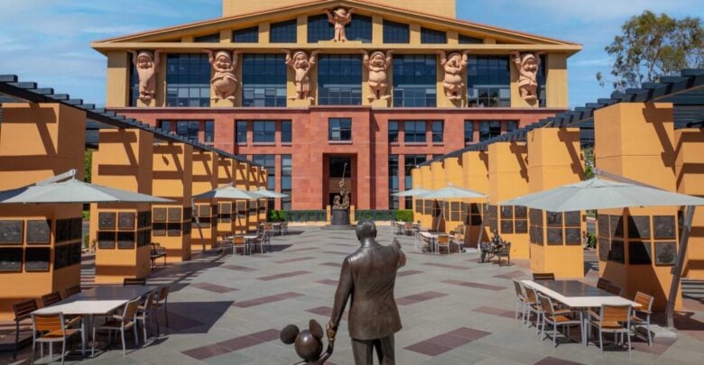 The Partners statue of Walt Disney and Mickey Mouse stands before the Seven Dwarfs building with outdoor seating at Disneyland.