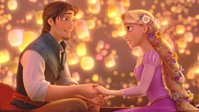 Rapunzel and Flynn Rider holding hands in a lantern-lit boat on the Tangled float during the Disney nighttime parade.