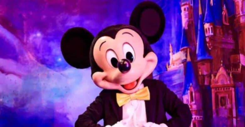 Mickey Mouse in a tuxedo with a yellow bow tie stands smiling before a colorful, magical backdrop featuring the iconic castle at Shanghai Disney Resort.