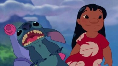 Lilo in her signature red dress stands with Stitch, mouth open in excitement, under the night sky at a Disney park.