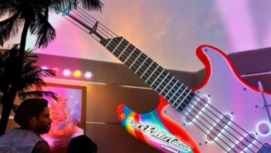 Fans gather by the giant, glowing guitar sculpture at Disney, celebrating the debut of Muppet Rock 'n' Roller Coaster under palm trees.