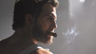 Henry Cavill’s Wolverine, rugged in a tank top with tousled hair and beard, smoking a cigar under moody lighting, MCU-style.