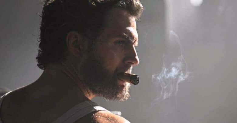 Henry Cavill’s Wolverine, rugged in a tank top with tousled hair and beard, smoking a cigar under moody lighting, MCU-style.