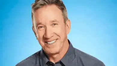 Guest resembling Tim Allen from Home Improvement Reboot, grinning in a blue shirt against a vivid blue theme park backdrop.