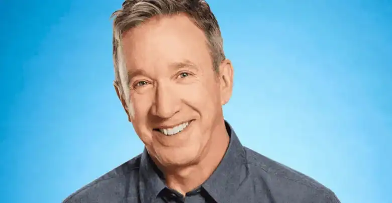 Guest resembling Tim Allen from Home Improvement Reboot, grinning in a blue shirt against a vivid blue theme park backdrop.