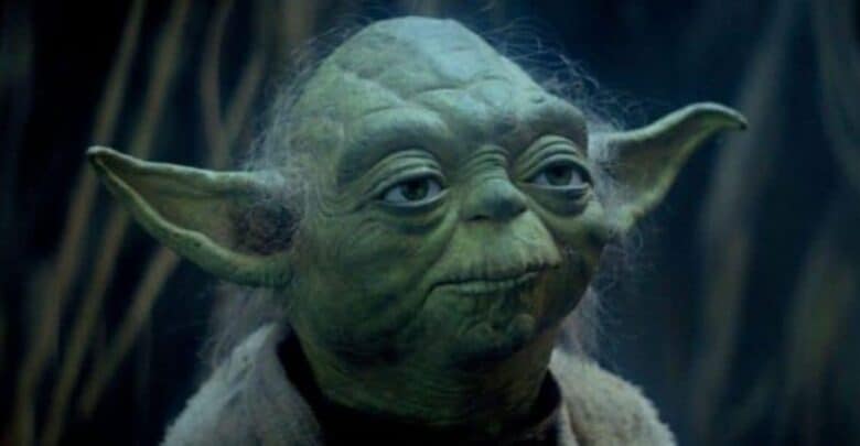 Yoda from Star Wars gazes ahead with wisdom in his eyes, surrounded by a dimly lit, forest-themed area evocative of the immersive settings found in a Star Wars attraction.