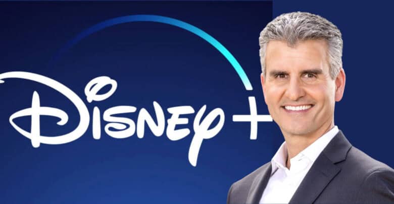 A sharply dressed Disney executive stands confidently before the glowing Disney+ logo on a vibrant blue backdrop, capturing the excitement and innovation fans associate with the new era of Disney entertainment and theme park experiences.