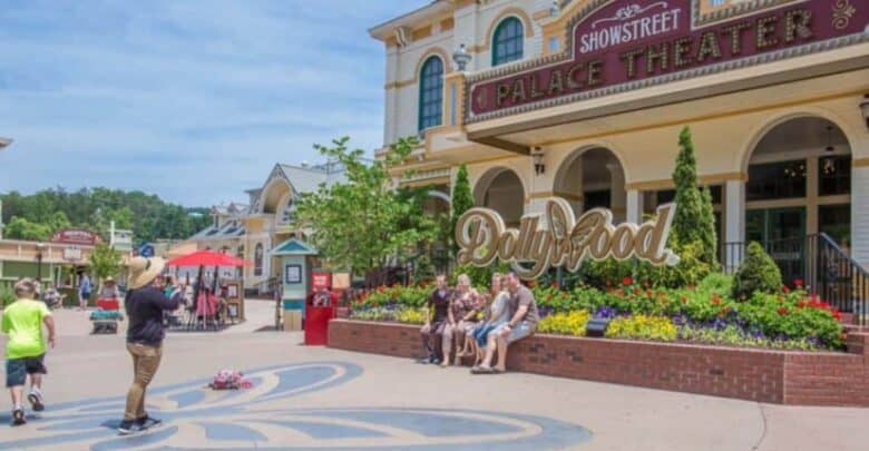 Fans gather in front of the iconic Dollywood sign, framed by vibrant flower beds and the park’s signature theater, capturing memories that honor Dolly Parton’s legendary influence at her celebrated theme park.