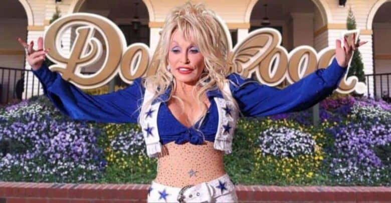 Dolly Parton in front of the iconic Dollywood sign, dressed in a sparkling blue outfit adorned with white stars, celebrating her signature musical style and charm.