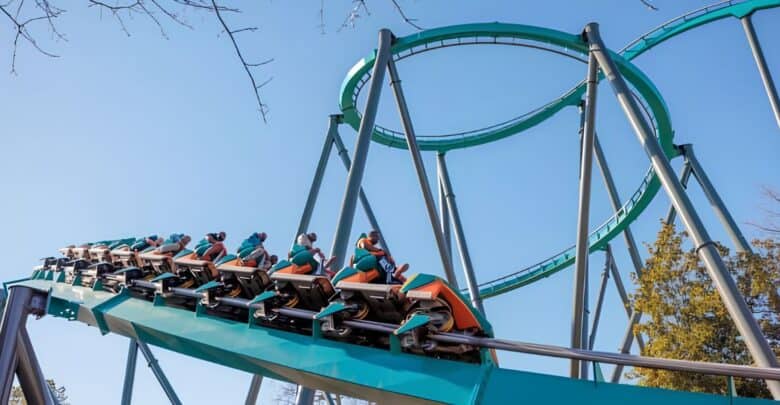 A Six Flags roller coaster train climbs the lift hill toward a massive loop.