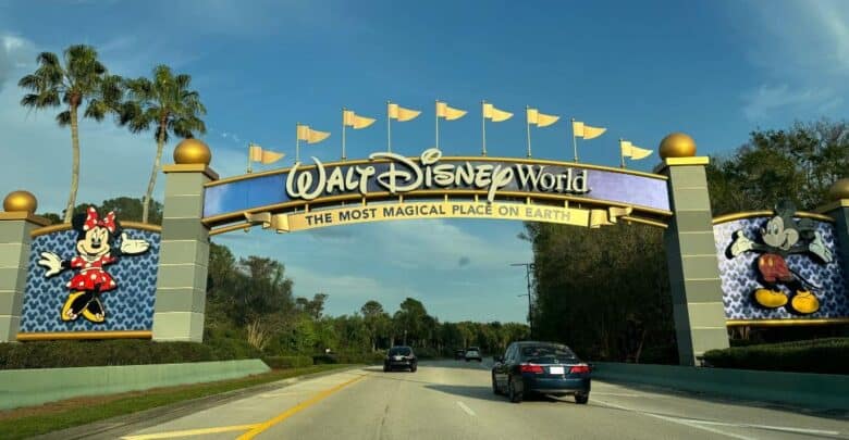 Cars driving under the Walt Disney World entrance archway featuring Mickey and Minnie Mouse as guests depart.