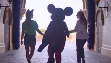 Mickey Mouse walks through the Cinderella Castle archway at Disney World holding hands with two guests involved in recent incidents.