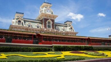 Main Street, U.S.A. train station at the Magic Kingdom entrance, featuring the iconic Mickey Mouse flowerbed in the foreground.