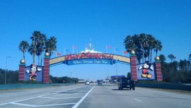 Minnie and Mickey Mouse standing before the Walt Disney World entrance archway.