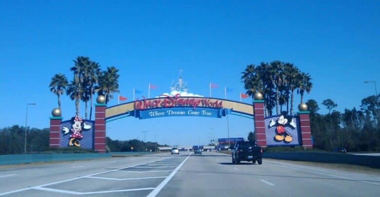 Minnie and Mickey Mouse standing before the Walt Disney World entrance archway.