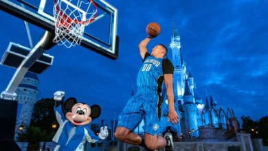 Orlando Magic player Aaron Gordon dunks a basketball in front of Mickey Mouse and Cinderella Castle at Disney World.