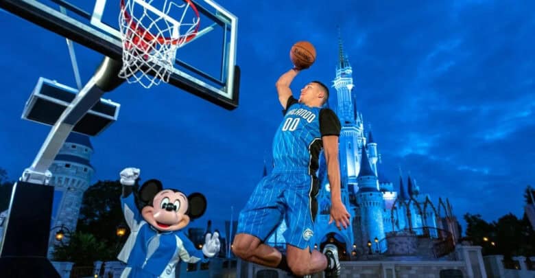 Orlando Magic player Aaron Gordon dunks a basketball in front of Mickey Mouse and Cinderella Castle at Disney World.