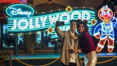 A couple takes a selfie in front of the neon sign for Disney Jollywood Nights at Disney’s Hollywood Studios.