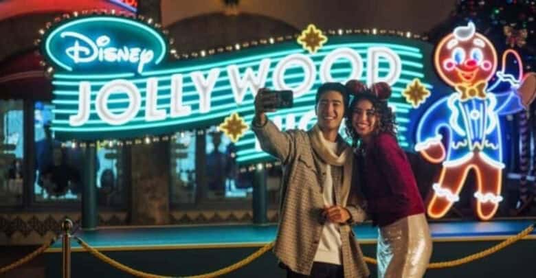 A couple takes a selfie in front of the neon sign for Disney Jollywood Nights at Disney’s Hollywood Studios.