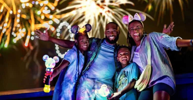 An annual passholder family wears Minnie ears and poses with light-up wands during Disney fireworks.