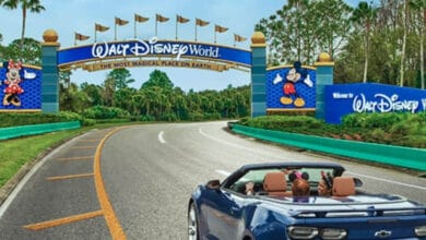A convertible drives through the Walt Disney World entrance archway featuring Mickey and Minnie Mouse.