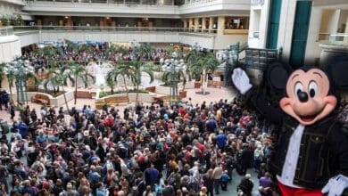 Mickey Mouse waving to guests in a crowded Orlando International Airport atrium.