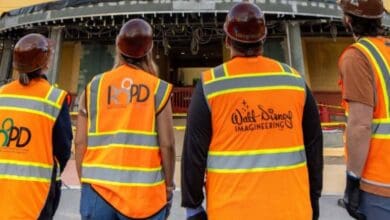 Walt Disney Imagineers in hard hats and safety vests at a theme park construction site.