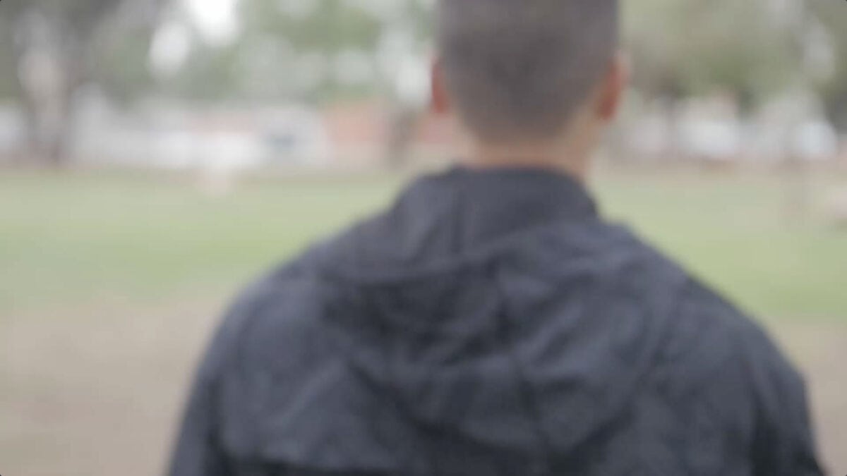 A guest in a black jacket explores the park, seen from behind with colorful trees and attractions softly blurred in the background.